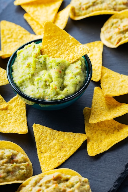 Guacamole and nachos chips on a dark background. Guacamole sauce with corn chips on a slate board. Close-up. Selective focus