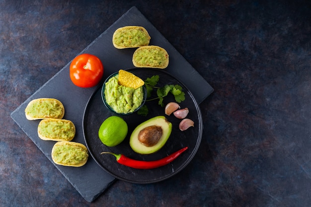 Guacamole saus, nachos chips en ingrediënten op een donkere achtergrond