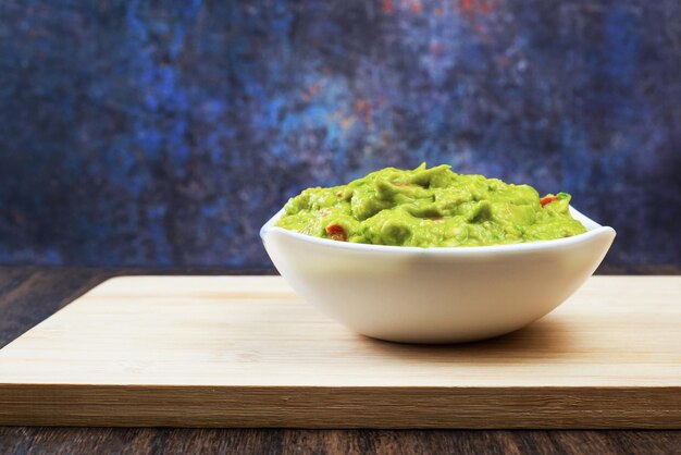 Guacamole served on white plate on wooden table. Isolated container with guacamole.