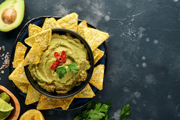 Photo guacamole. traditional latinamerican mexican dip sauce in a black bowl with avocado and ingredients and corn nachos