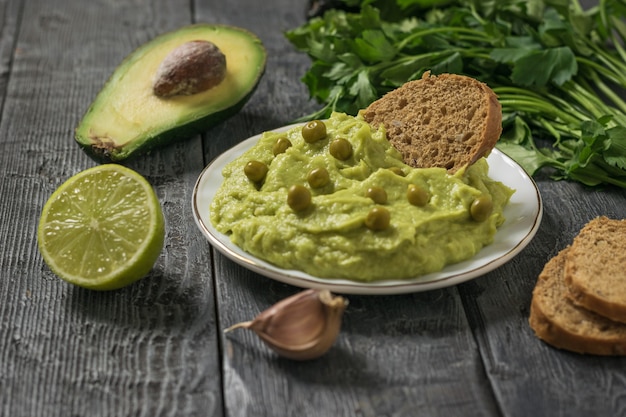 Guacamole con piselli, prezzemolo e lime in un piatto bianco su un tavolo di legno. dieta vegetariana cibo messicano avocado. cibo crudo.