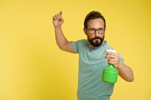 Foto in guardia della freschezza refresh concept uomo barbuto con occhiali rinfrescare acqua spruzzata uomo rinfrescare con bottiglia spray sfondo giallo tempo per rinfrescarsi stagione calda caldo e sete