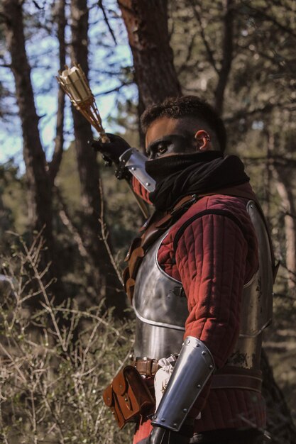 Photo guerrero medieval en el bosque, llevando una espada y una antorcha.