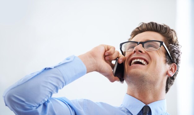 내가 방금 그 큰 고객을 만났는지 맞춰보세요. 흥분한 젊은 사업가가 미소를 지으며 휴대폰 통화를 하고 있습니다.