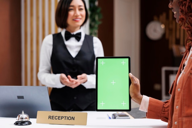 체크인 시 그린스크린을 사용하는 고객은 리셉션 직원에게 호텔 서비스에 대해 이야기하고 태블릿을 들고 있습니다.