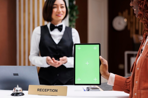 チェックイン時にグリーンスクリーンを使用し、タブレットを持ちながらホテルのサービスについて受付係に話すゲスト