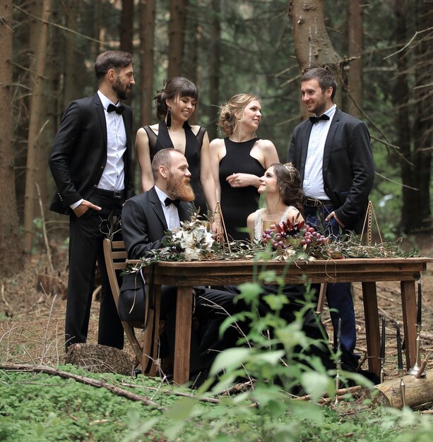 Guests and a couple of newlyweds near the picnic table in the woods.