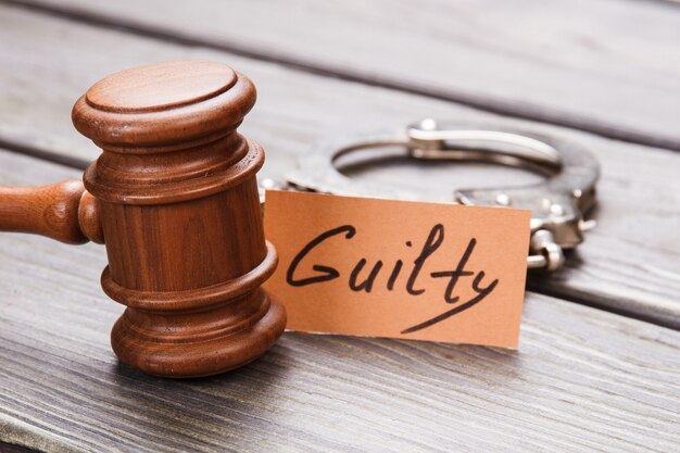 Guilty and crime concept. Close-up brown wooden gavel with handcuffs on wooden desk.