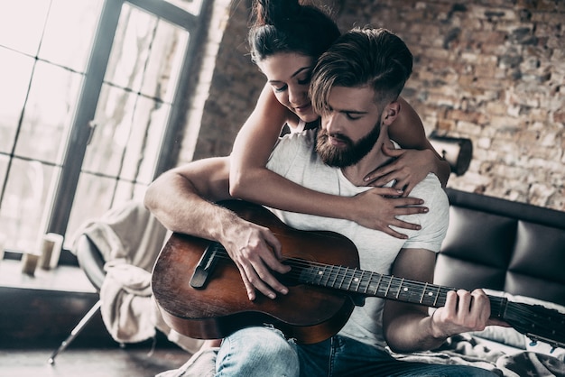 Guitar fun. handsome young bearded man sitting in bed at home and playing guitar