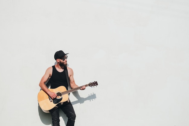 Guitar player singing outside. Hipster guitar player with beard and black clothes