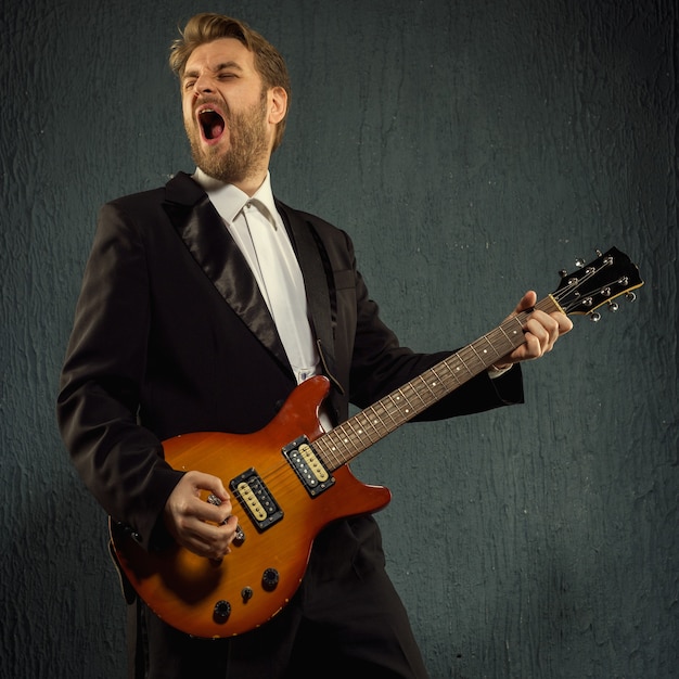 Guitar player with beard and black tailcoat emotionally plays music