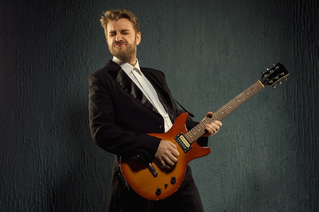 Guitar player with beard and black tailcoat emotionally plays music