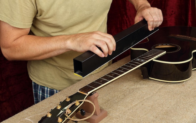 Guitar repair and service worker grinds black guitar neck\
frets