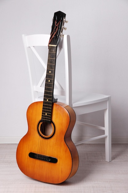 Гитара на белом деревянном стуле на полу на белом фоне