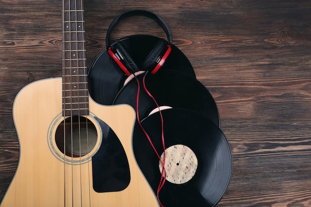 Guitar with vinyl records and headphones on wooden table close up