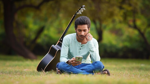 公園で携帯電話を使用してギタリストの少年