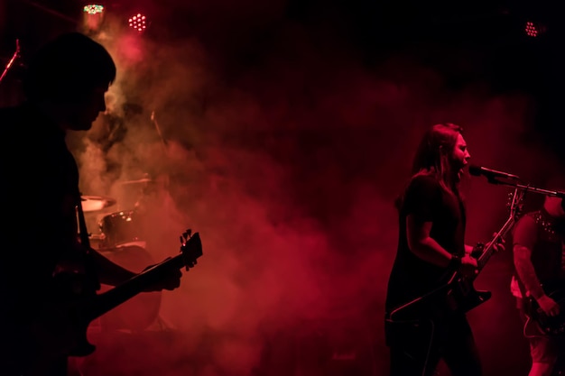 ギタリストがマイクに向かって歌い、コンサートのステージで煙の中で赤い音色で演奏します