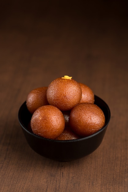 Gulab Jamun in bowl on wooden background.