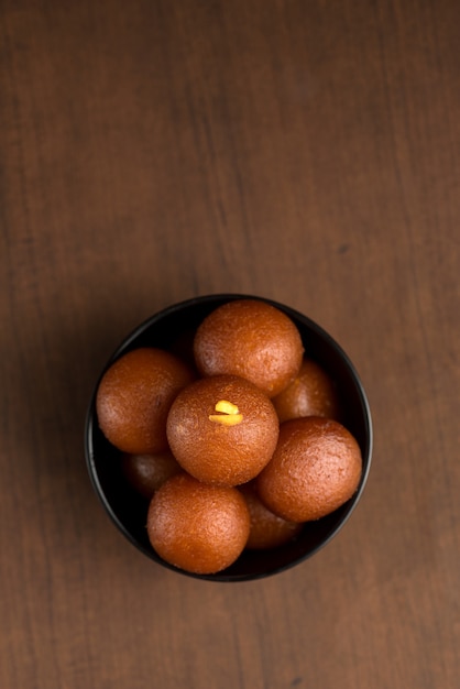 Gulab Jamun in bowl on wooden background.