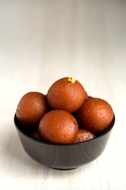 Gulab Jamun in bowl on wooden background.