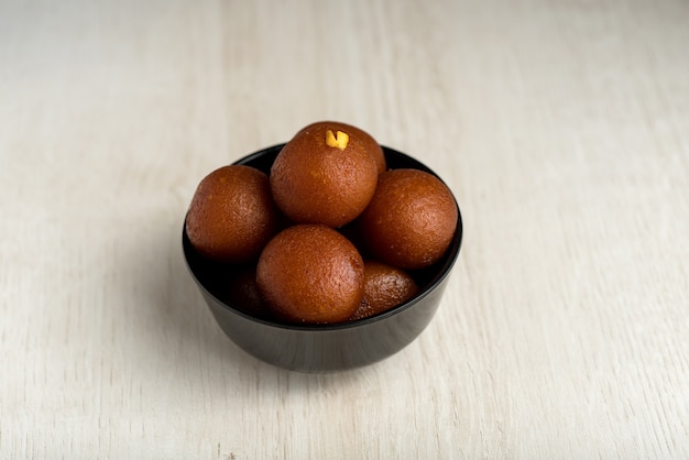 Gulab jamun nella ciotola su sfondo di legno.