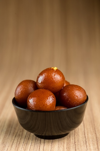 나무 배경에 그릇에 Gulab Jamun입니다.