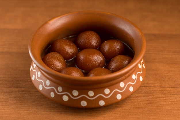 Gulab Jamun in clay pot with spoon and dry fruits. Indian Dessert or Sweet Dish