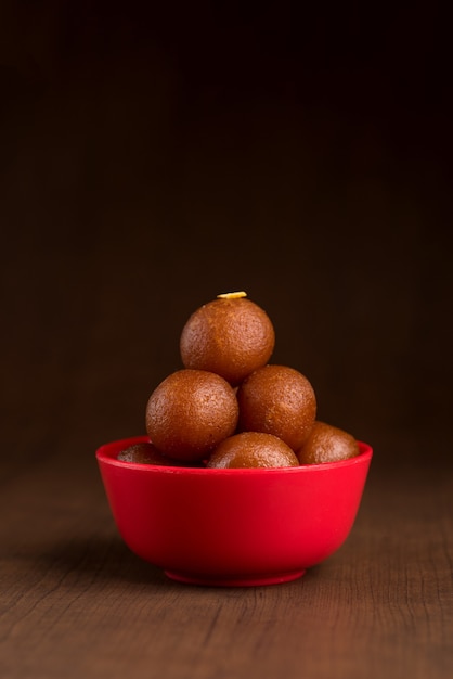 Gulab jamun in rode kom op houten achtergrond. indiase dessert of zoete schotel.