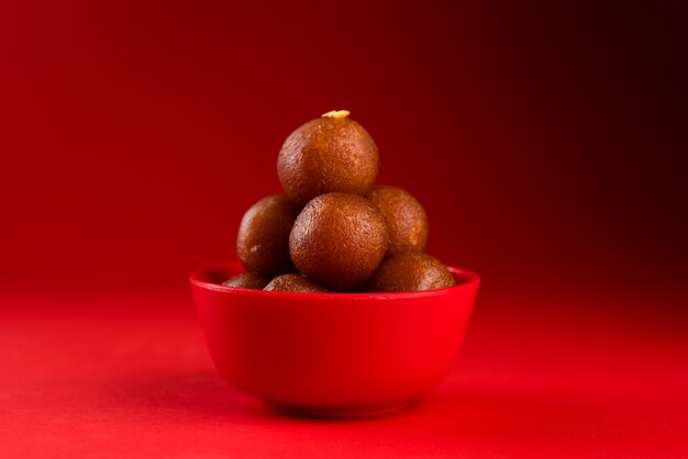 빨간색 바탕에 빨간색 그릇에 Gulab Jamun입니다. 인도 디저트 또는 달콤한 요리.