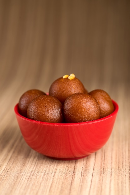 Foto gulab jamun nella ciotola rossa su legno. dessert indiano o piatto dolce.