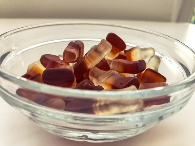 Gummy candies in the form of lemonade bottles are in a round transparent bowl appetizing sweets