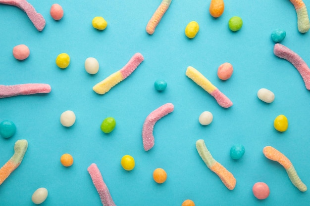 Gummy worm candies and pills on blue background. Top view