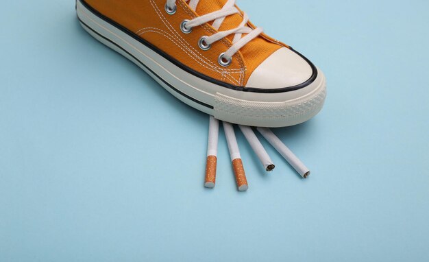 Gumshoe sneaker stepped on cigarettes on a blue background.\
quitting smoking concept