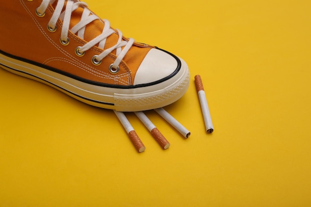 Gumshoe sneaker stepped on cigarettes on yellow background.\
quitting smoking concept