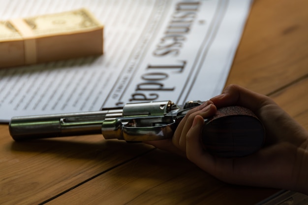 Photo gun in hand with blur soft background of banknotes and newspapers on wooden table