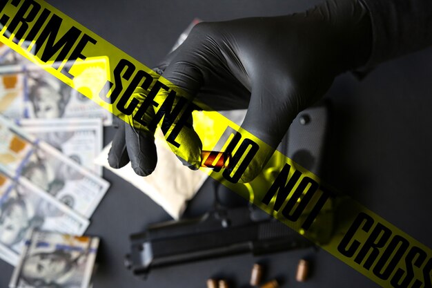 Gun lying on the table. Man in black gloves holding bullets. Illegal drug selling. Crime scene do not cross tape. Dollars.