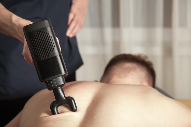 Gun percussion massage back muscle athletic man in medical room