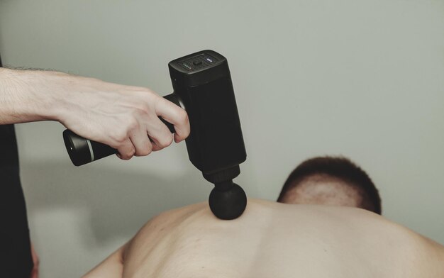 Фото Пистолетная перкуссия массирует мышцы спины спортсмену в медицинском кабинете в спортзале