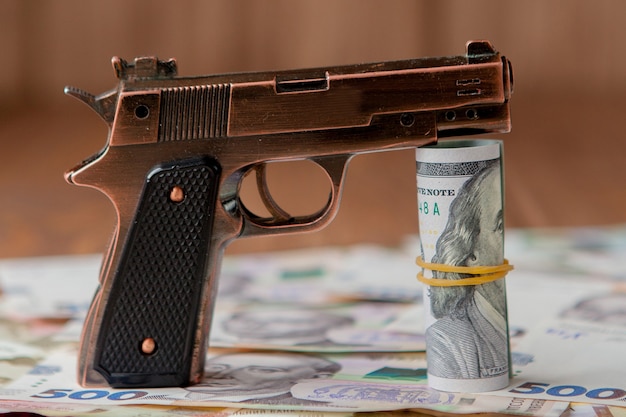 Gun and Stack of Money lying on the hryvnia on a wooden table. Drug use, crime, addiction and substance abuse concept