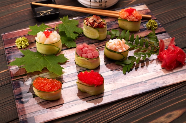 Photo gunkan maki in a cucumber, with caviar, tuna. scallop, eel, shrimp, eel and salmon, on a wooden board