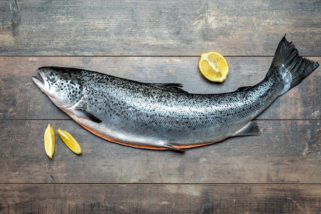 内臓を取り除いたマスの枝肉は、暗い背景の木に新鮮な生サーモン赤魚をレモンで切るための木の板にあります。海の魚の健康食品