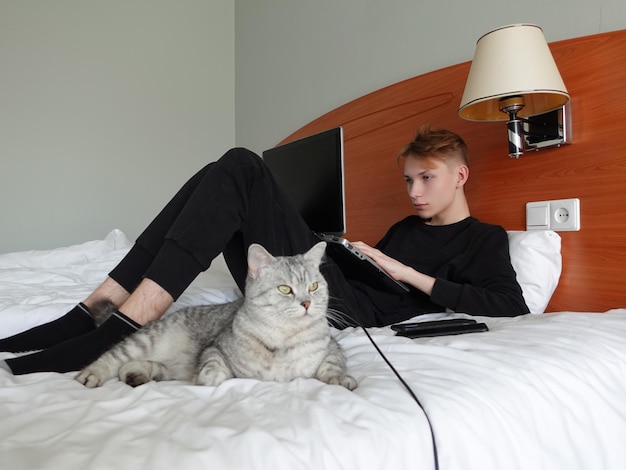 The guy on the bed with a laptop Next to him lies a gray cat Hotel or apartment