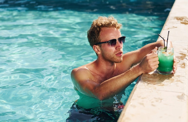 Guy in black sunglasses and with cocktail is in swimming pool