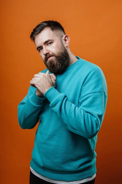 A guy in a blue sweater looks at the camera holding his hands together in front of him