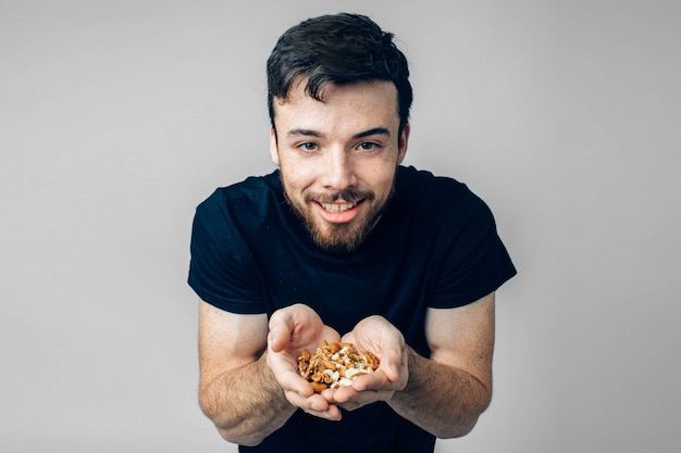 Guy in casual black clothes hold different nuts in hands and smile