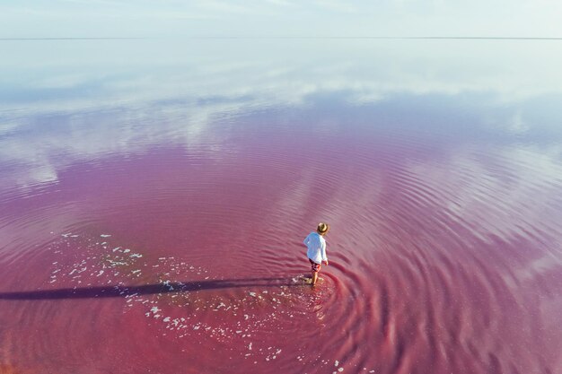 カジュアルな服装の男はピンクと紫の色の浅い水の中を散歩します