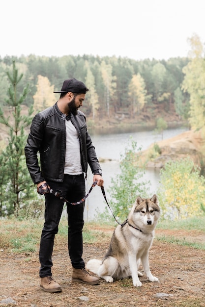 Guy in casualwear holding leash of his purebred pet during chill in rural environment at leisure