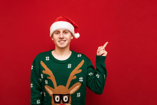 Photo guy in christmas clothes points his finger at copy space and laughs