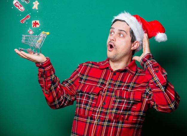 Guy in Christmas hat and tartan shirt with shopping cart on green