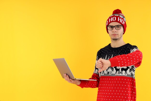 Guy in Christmas sweater with laptop on yellow background